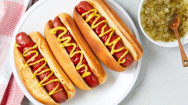 a plate with 3 hot dogs covered in mustard and a side of relish in a bowl