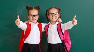 girls dressed up as twins with a black skirt, white shirt, red backpacks and black glasses