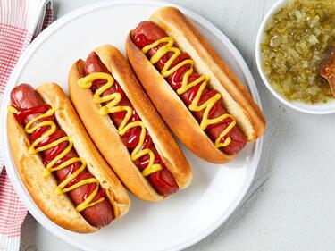 a plate with 3 hot dogs covered in mustard and a side of relish in a bowl