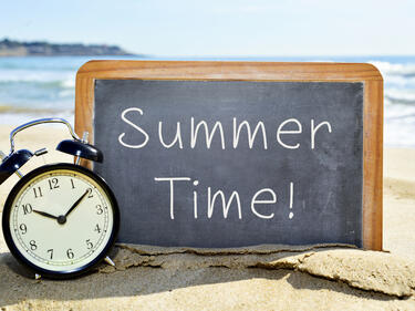 a beach with a sign and clock for summer time