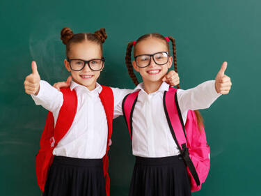 girls dressed up as twins with a black skirt, white shirt, red backpacks and black glasses
